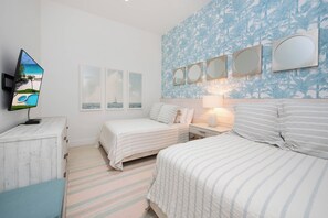 A hotel room with two beds, a TV, and a wall with framed pictures. - Beachcomber 39 by Grand Cayman Villas (7 Mile Beach)