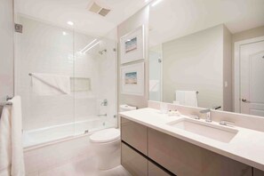 A modern bathroom with a glass shower enclosure, a white sink, and a large mirror. - Beachcomber 12 by Grand Cayman Villas (7 Mile Beach)