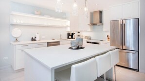Eine moderne Küche mit weißen Schränken, einem Edelstahlkühlschrank und Pendelleuchten.