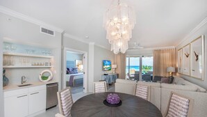 Ein modernes Wohnzimmer mit einem runden Esstisch, einer Chandelierleuchtre und Meerblick.