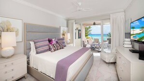 Ein Hotelzimmer mit Bett, Fernseher, Schreibtisch und einem Balkon mit Blick auf den Strand.