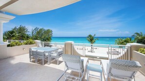 A balcony with a view of the ocean, outdoor furniture, and a pool area.