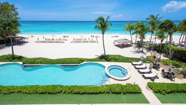 A resort with a swimming pool, beach, and palm trees.