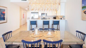 A modern dining area with a glass-top table, blue chairs, and a decorative chandelier.