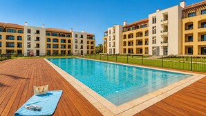A swimming pool with a wooden deck, surrounded by multi-story buildings with balconies. - ANDIAMO GARDENS APARTMENT (Vilamoura)