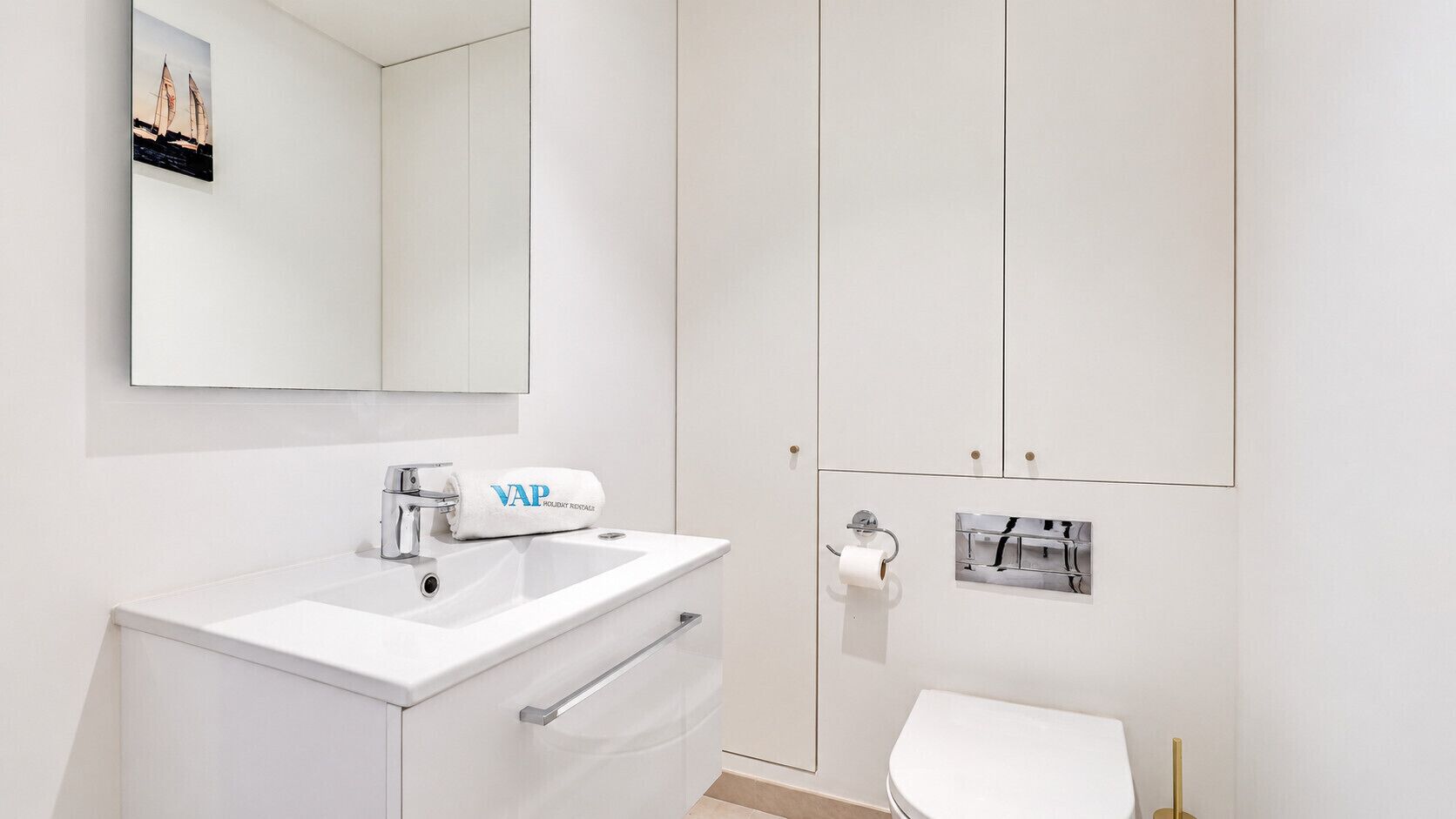 A modern bathroom with a white sink, a towel with 'VAP' branding, a toilet, and a mirror.