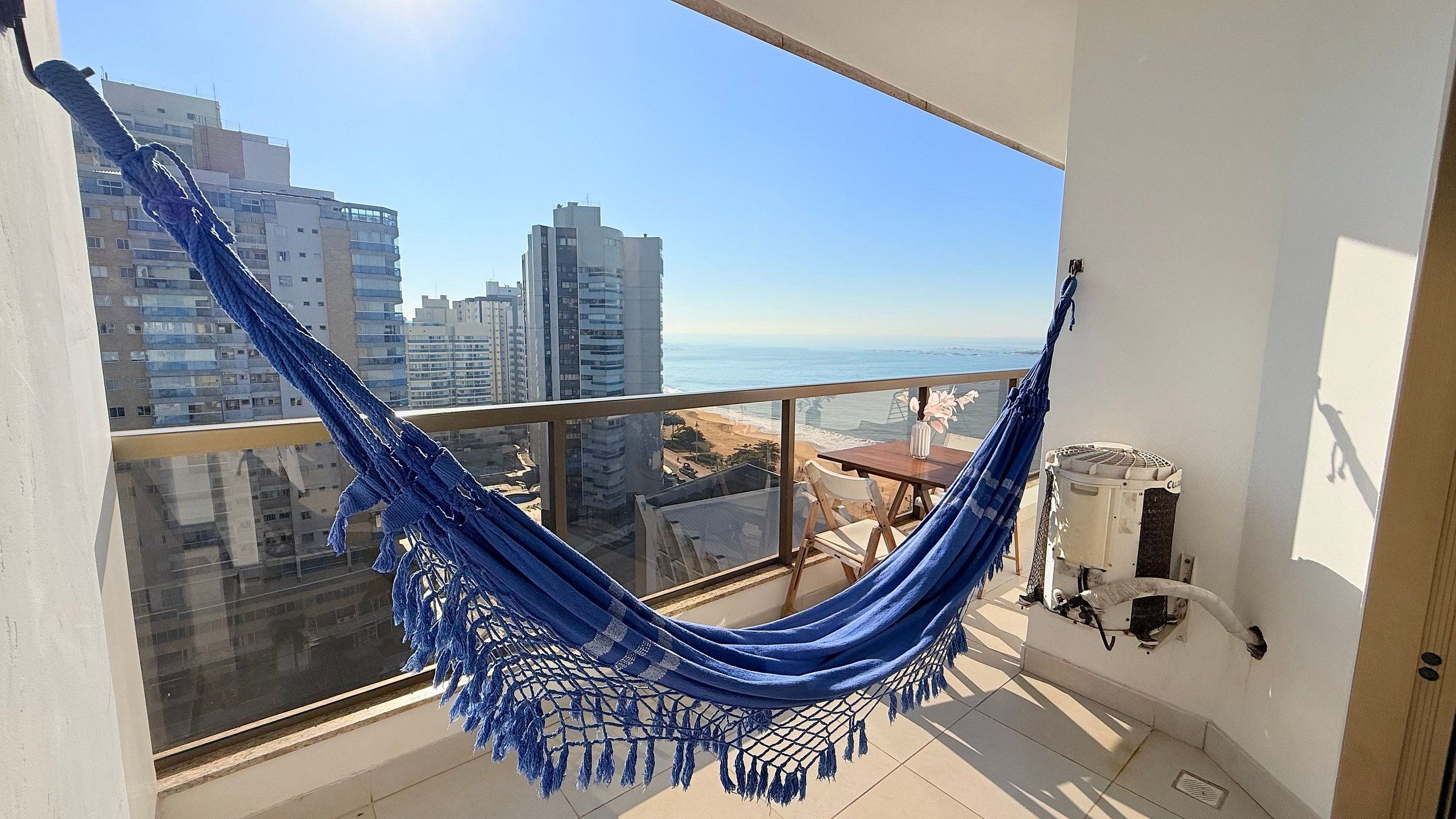 A balcony with a hammock, a view of the ocean, and a cityscape.