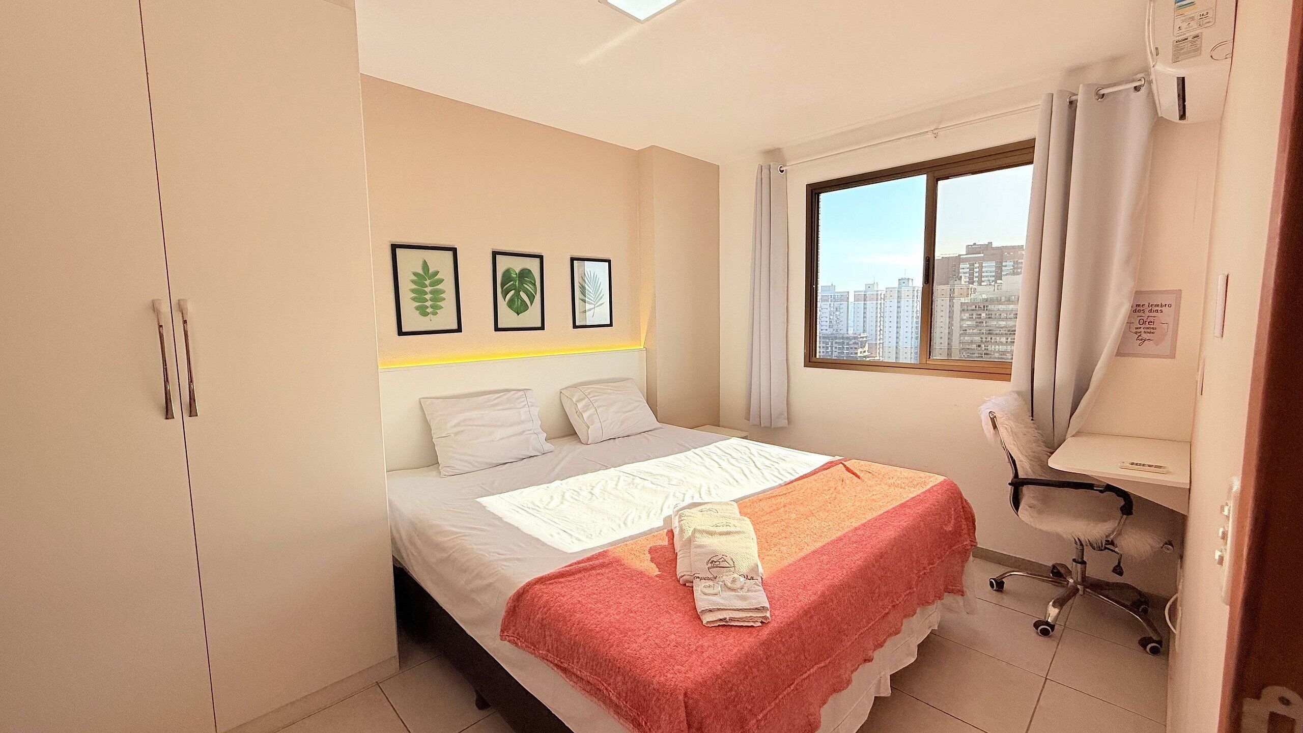 A bedroom with a bed, a desk, a chair, and a window with a city view.