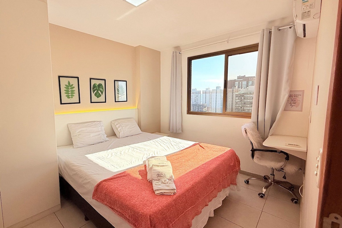 A bedroom with a bed, a desk, a chair, and a window with a city view.
