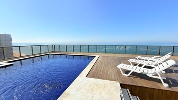 Una piscina infinita en la azotea con terraza de madera y sillones blancos.