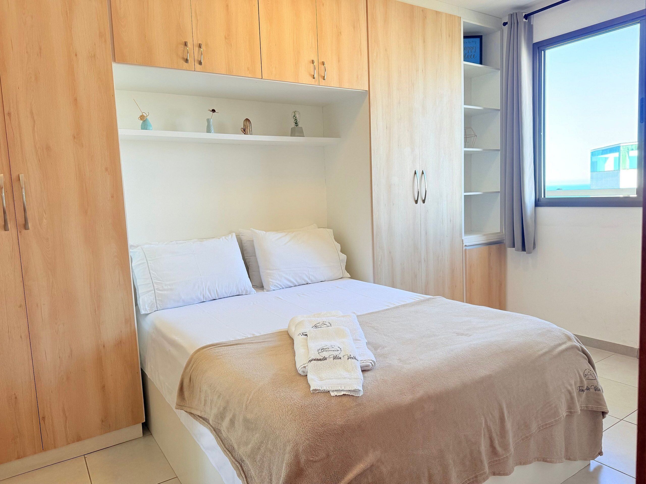 A bedroom with a bed, wooden wardrobe, and a window with curtains.