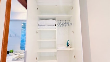 Un armario blanco con estantes, una barra para colgar ropa y una toalla doblada.
