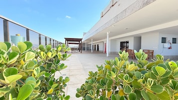 Un amplio espacio al aire libre con plantas en macetas, una zona de estar cubierta y vistas a un edificio moderno.