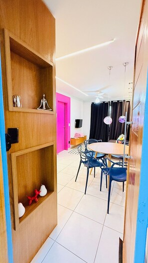 A modern living room with a dining area, wooden shelves, a pink door, and a ceiling fan. - Praia Dourada (Vila Velha)