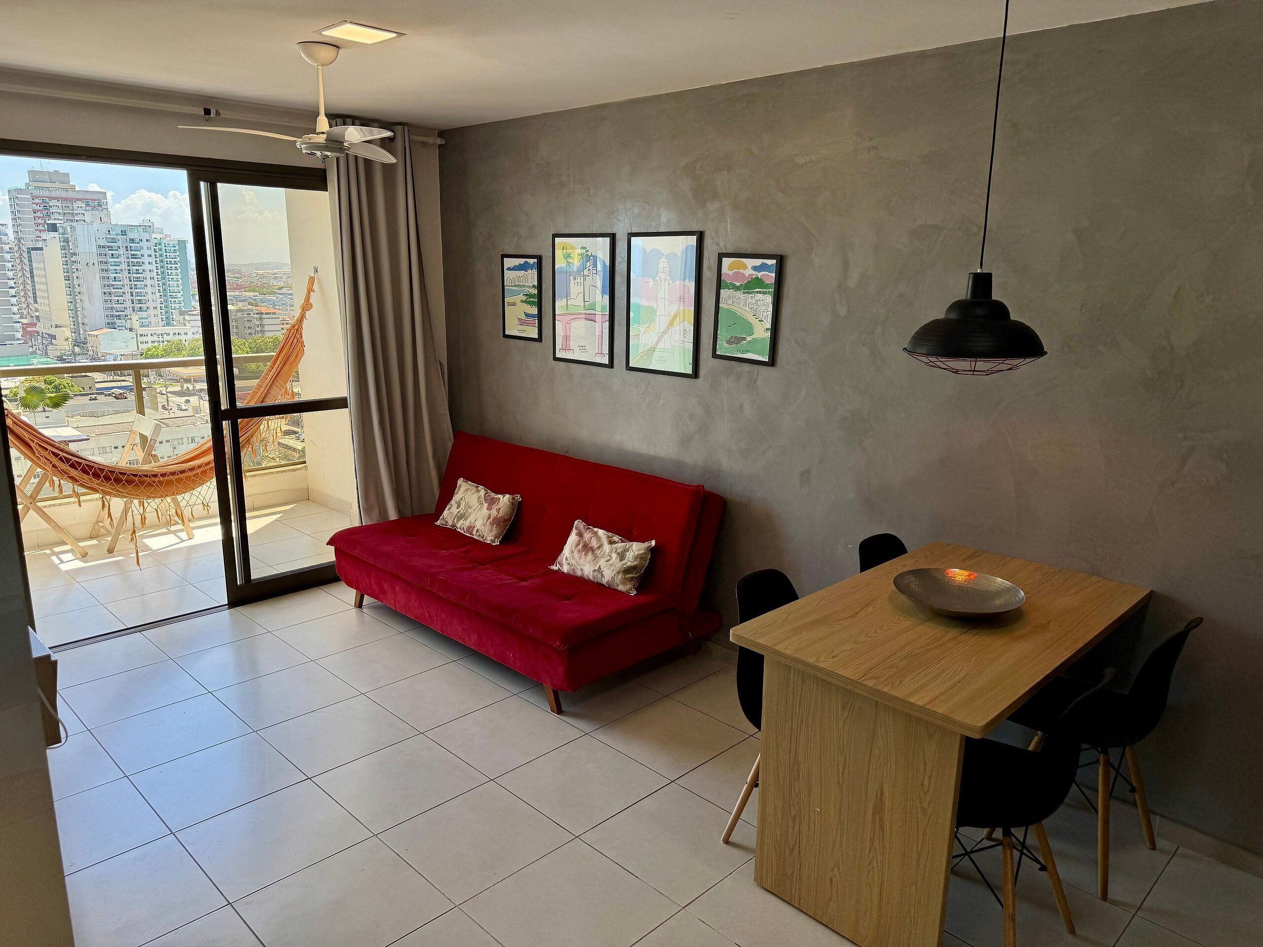 Un espacio habitable moderno con un sofá rojo, una mesa de comedor y vistas a la ciudad a través de amplias ventanas.