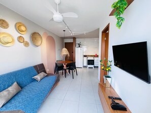 A modern living room with a sofa, dining table, chairs, a TV, ceiling fan, and a kitchen in the background. - Praia Dourada (Vila Velha)