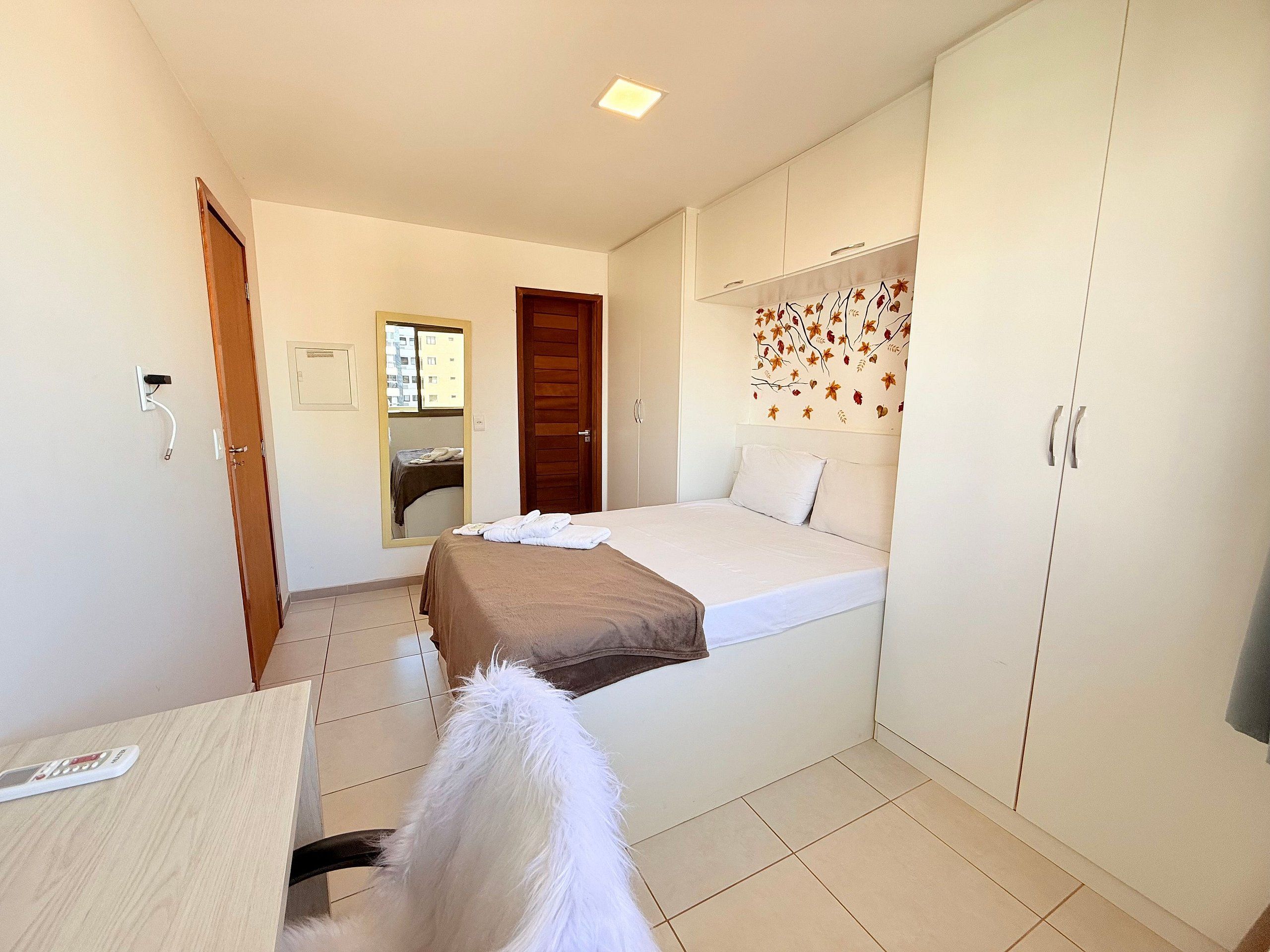 Ein Schlafzimmer mit Bett, Kleiderschrank, Spiegel und Schreibtisch mit Fernbedienung.