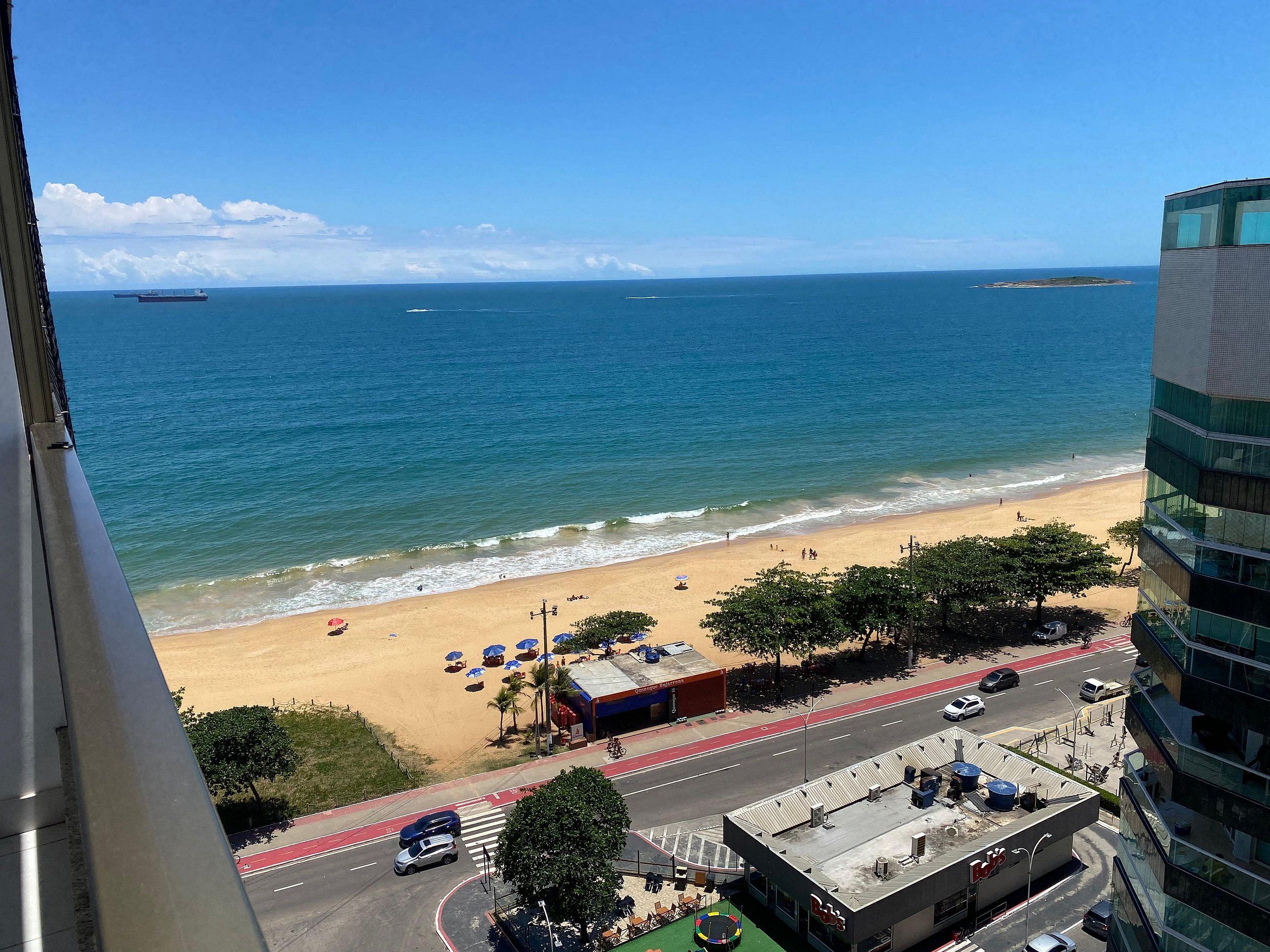 A coastal view with a beach, ocean, and a road with vehicles.