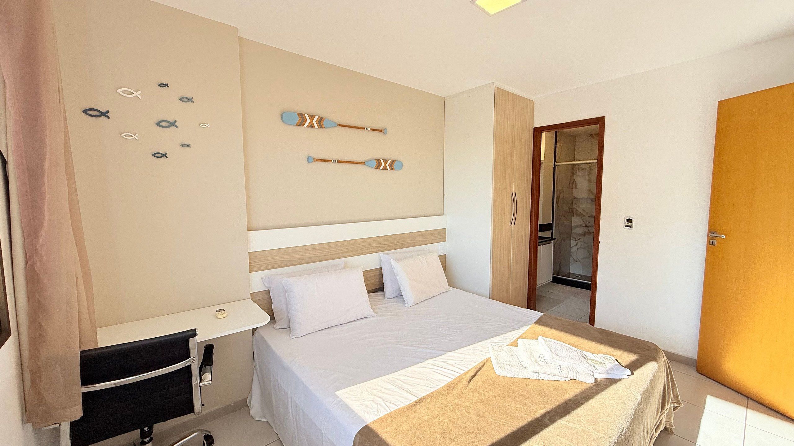 Une chambre à coucher comprenant un lit, une table de chevet, une horloge murale et une porte donnant accès à une salle de bain.