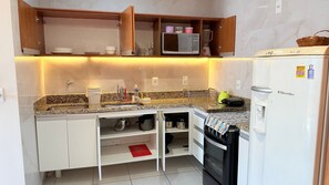 A compact kitchen with a microwave, refrigerator, and built-in oven. - Praia Dourada (Vila Velha)