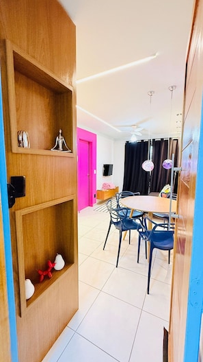 A modern living room with a dining area, wooden shelves, a pink door, and a ceiling fan. - Praia Dourada (Vila Velha)