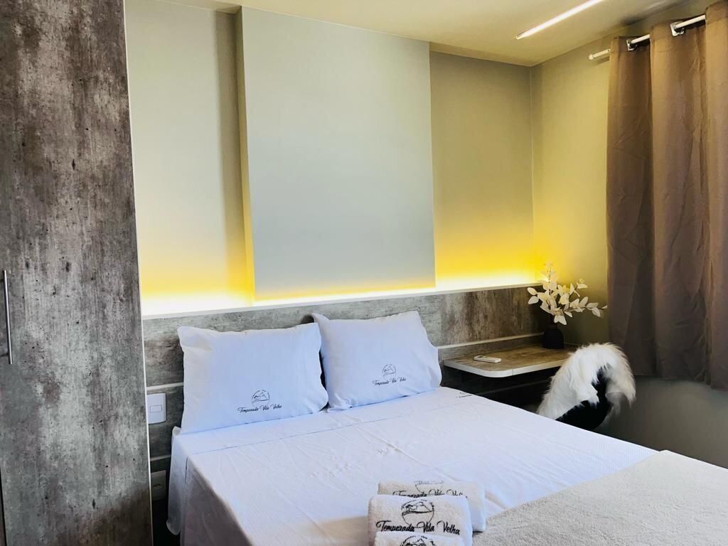 A hotel room with a bed, a nightstand, a lamp, and a window with curtains.