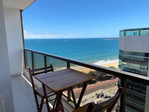 A balcony with a view of the ocean and a beach, a wooden table, and a chair. - Praia Dourada (Vila Velha)