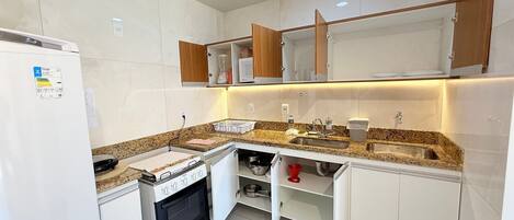 Una cocina compacta con armarios blancos, horno empotrado, encimera de granito y un lavabo.