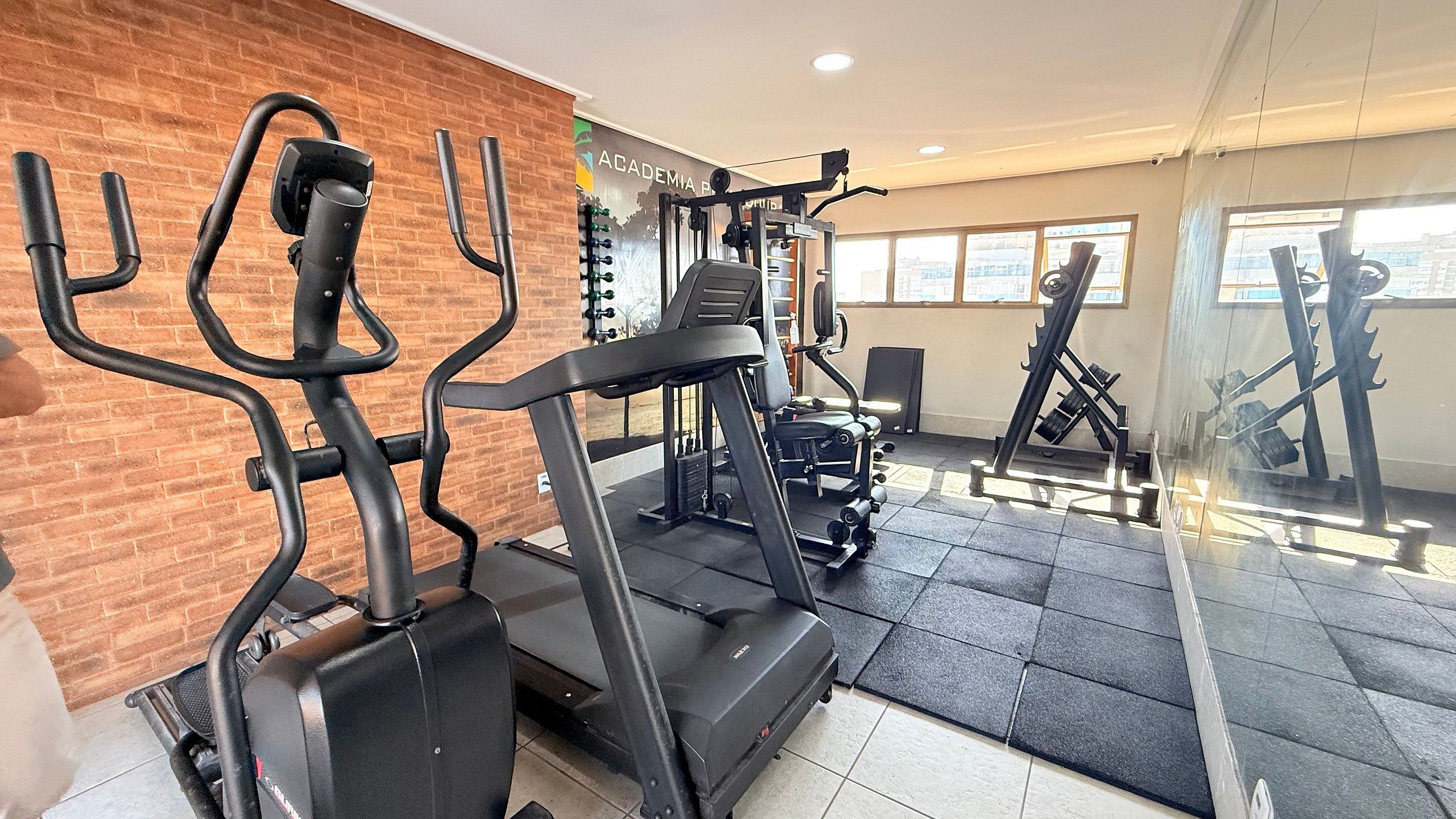 A gym with exercise equipment, a brick wall, and large windows.