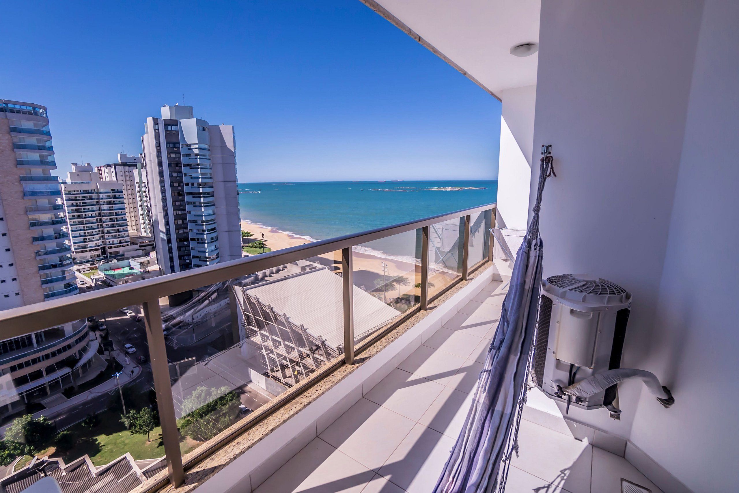 A balcony with a view of the beach and cityscape, a white wall, and a ceiling fan.