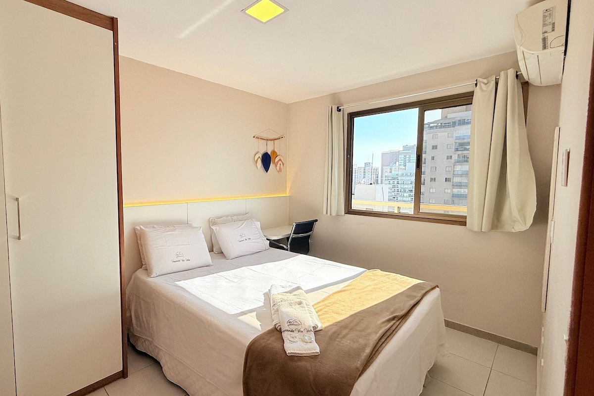 A hotel room with a bed, a wardrobe, a window with curtains, and a city view.