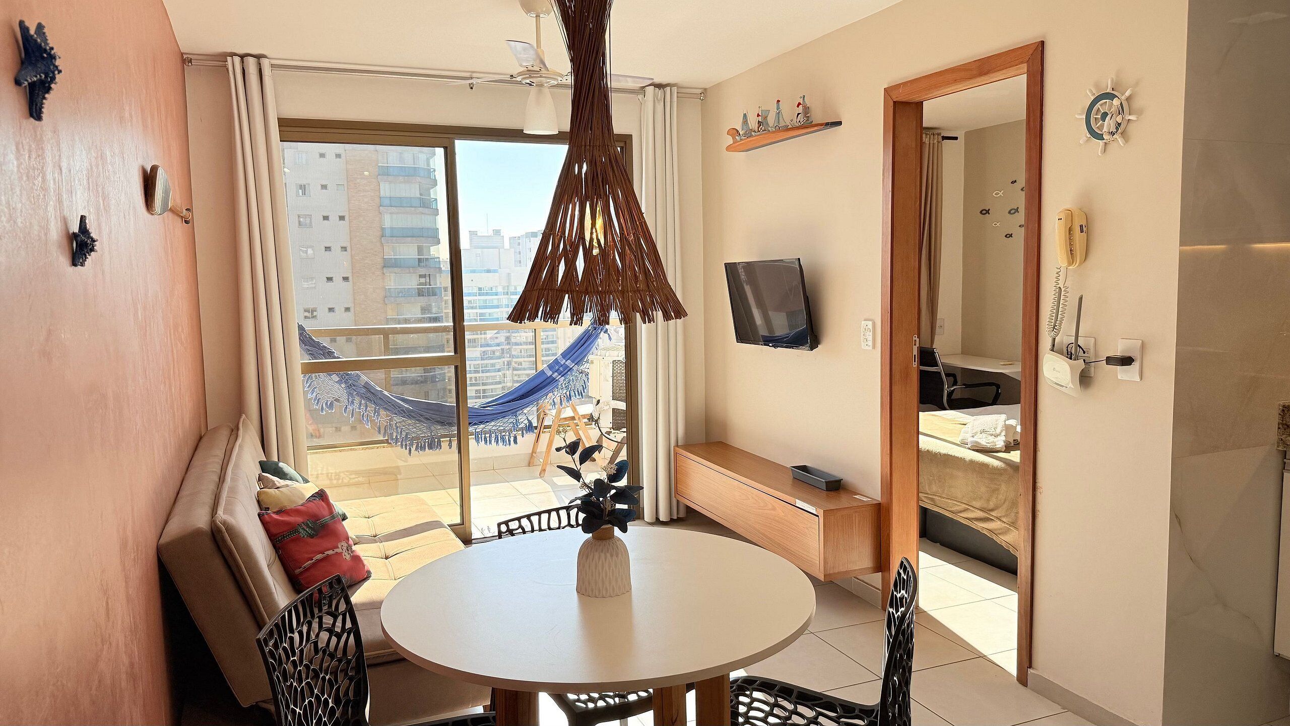 A modern apartment with a balcony, a dining area, a TV, and a bathroom.