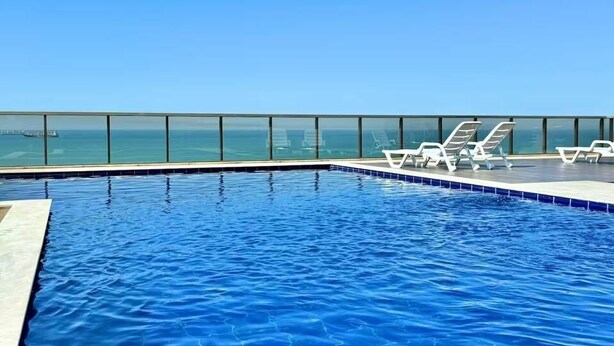 Une piscine d’un bleu éclatant, dotée de chaises longues et offrant une vue sur l’océan.
