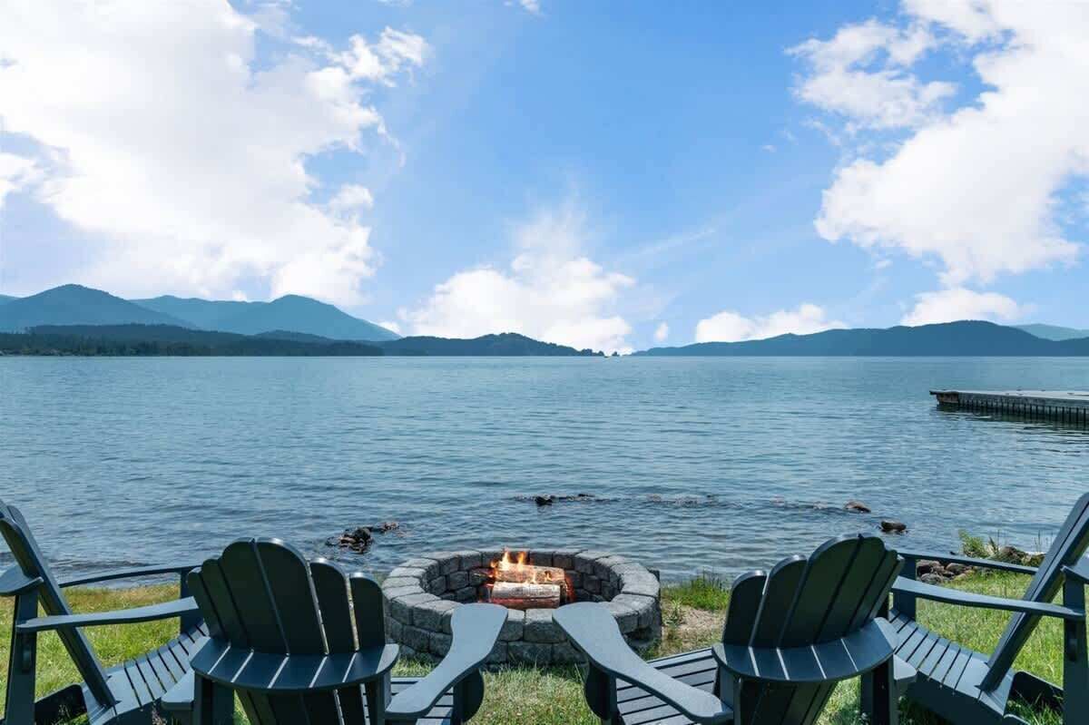 Une vue sur le lac, avec un foyer et des fauteuils Adirondack donnant sur un lac paisible, le tout entouré de montagnes.