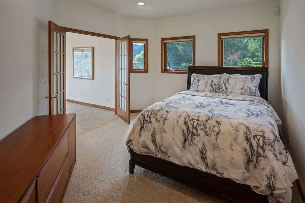 Une chambre à coucher comprenant un lit, une commode en bois et deux fenêtres donnant sur un paysage verdoyant.