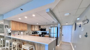 A modern kitchen with a large island, wooden cabinets, and a stainless steel refrigerator. - Seasational Escape!  Amazing Beachfront Condo/Covered Balcony, BEACH SER, Pool (Panama City Beach)