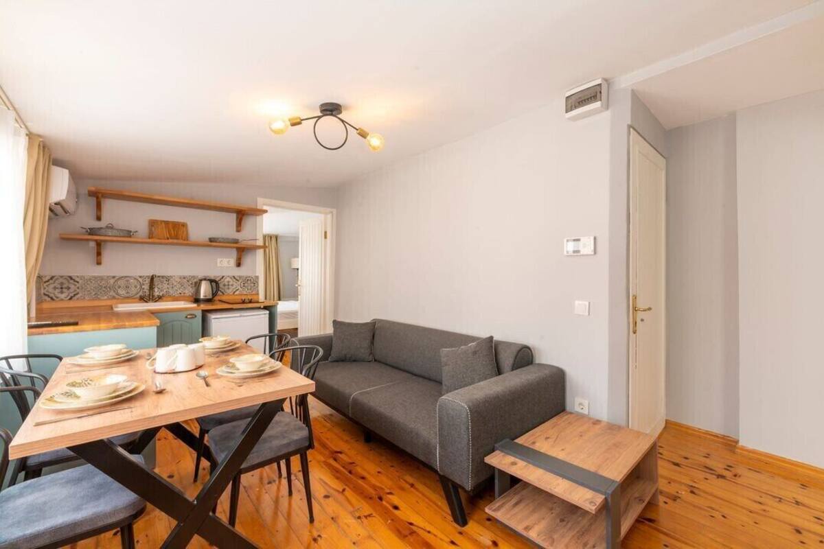 A compact living space with a dining area, a gray sofa, and a small kitchen area with wooden shelves.