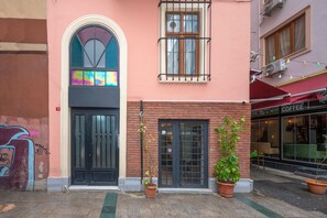 A building with a black door, a window with a colorful stained glass design, and a brick wall.