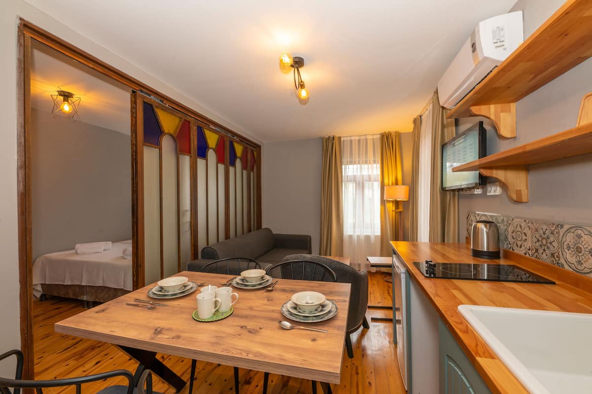 A compact room with a dining table set for two, a sofa, a bed, and a kitchenette with a microwave and kettle.