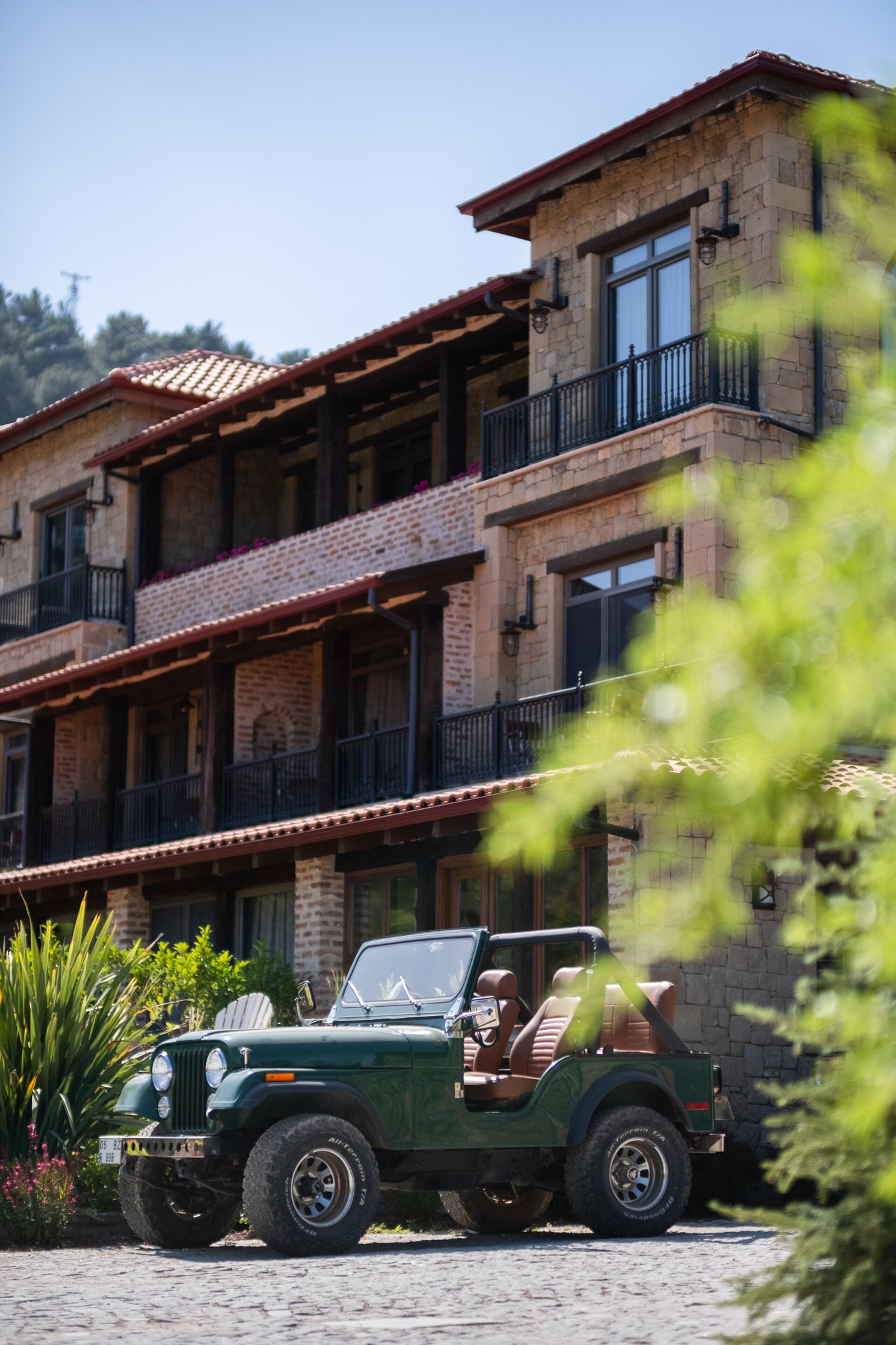 A green jeep parked in front of a multi-story building with balconies and a red-tiled roof.