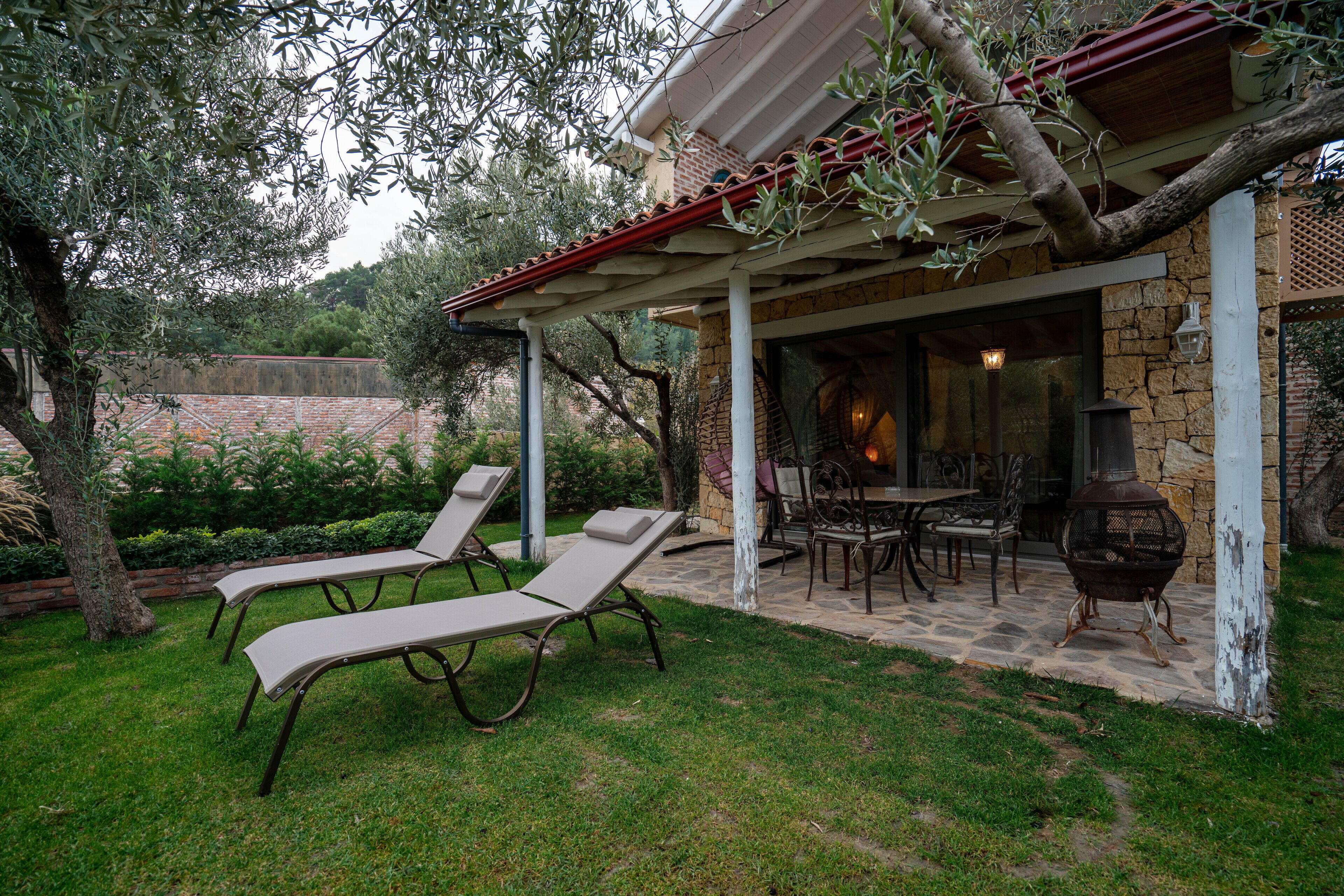 A covered outdoor patio with two lounge chairs, a stone table, and a grill.