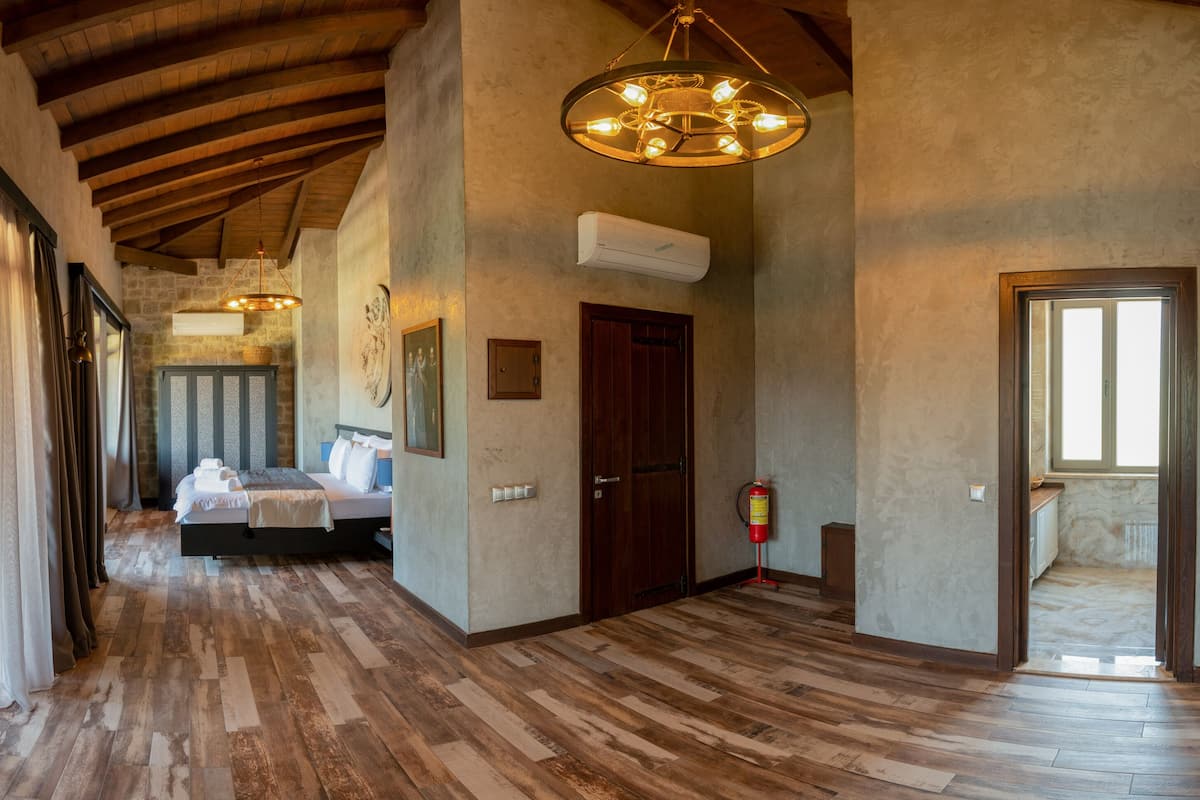 A hallway with wooden flooring, a bed in the background, and a chandelier.