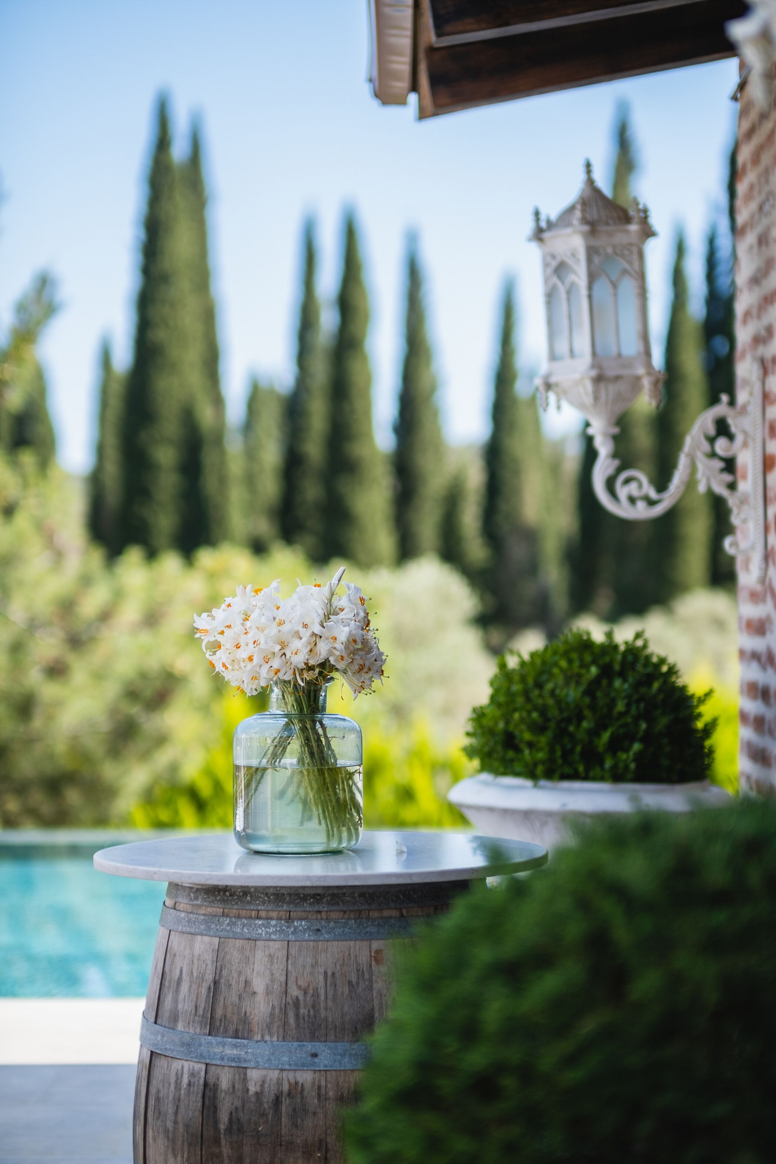 A wooden barrel with a vase of white flowers, a lantern, and a pool in the background.