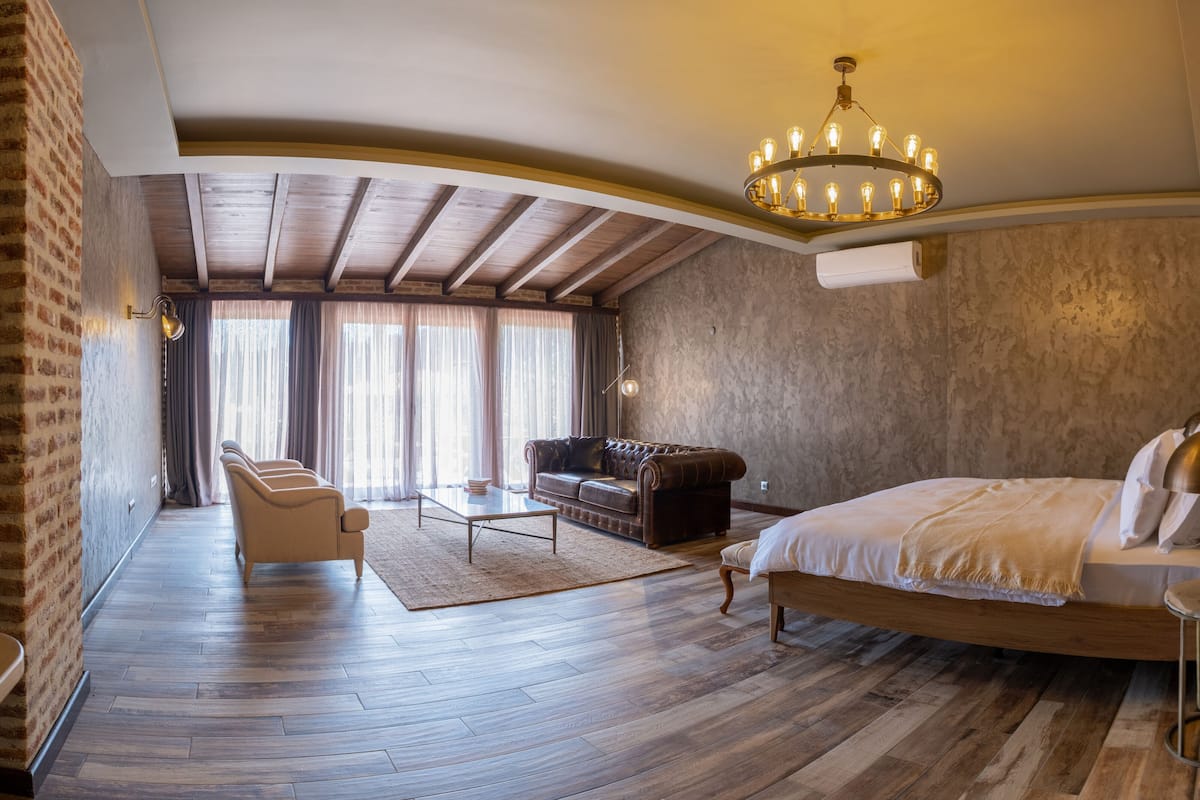 A spacious bedroom with a large bed, a leather sofa, and a wooden floor.