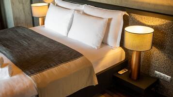 Een net opgemaakt bed met witte lakens en een grijze plaid, met aan beide zijden nachtkastjes met bijpassende bedlampen.