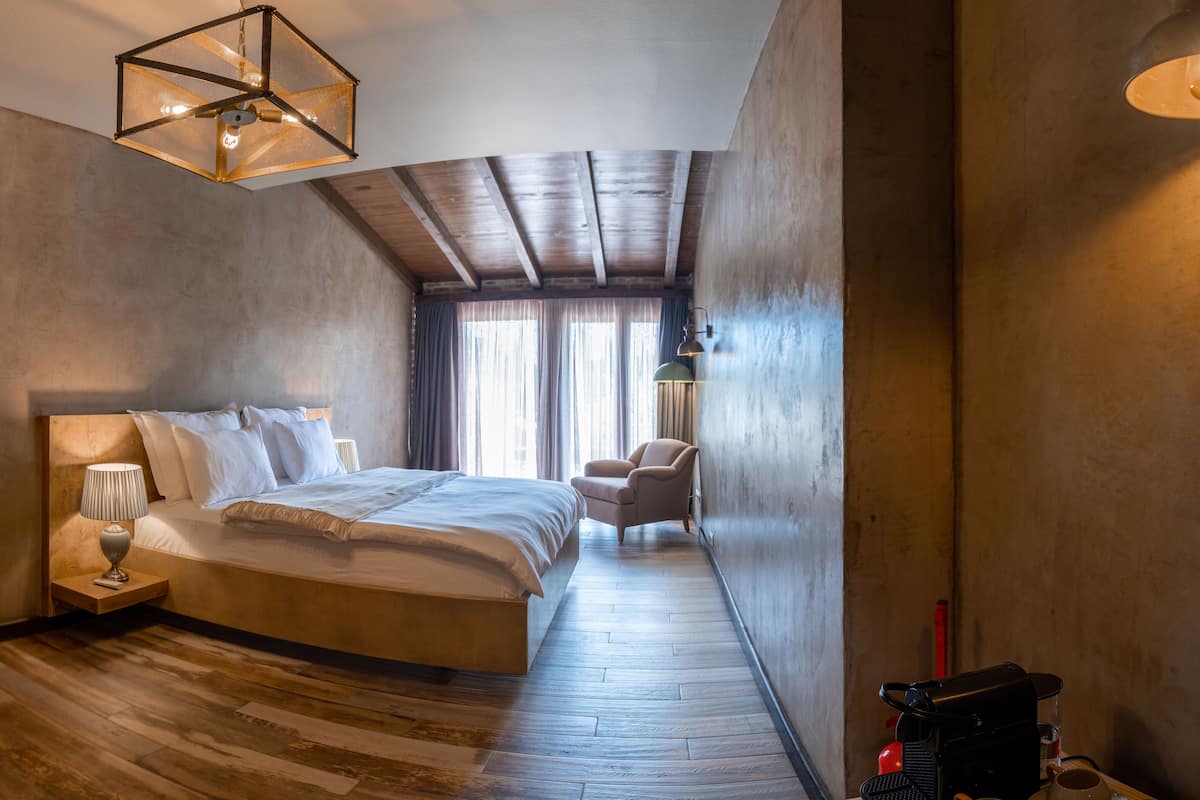 A bedroom with a wooden floor, a bed, a chair, a lamp, and a ceiling light fixture.