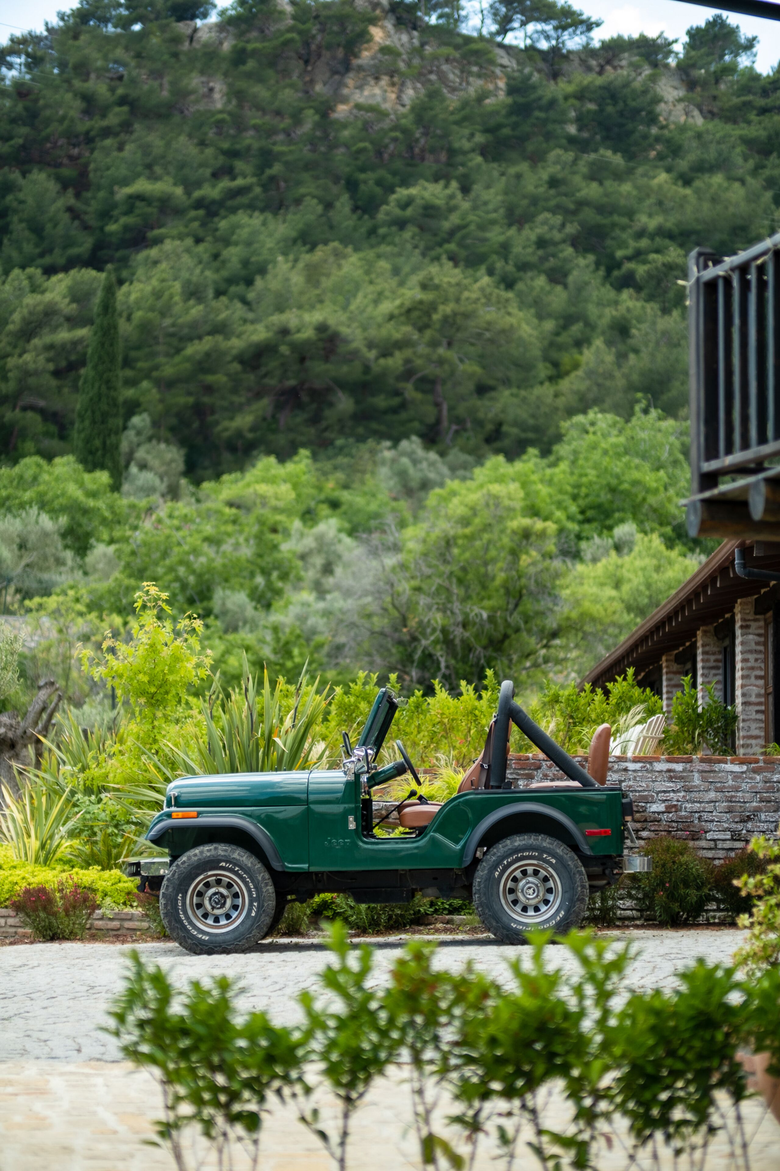 Un véhicule tout-terrain vert est garé devant un bâtiment à la façade en pierre, avec un paysage verdoyant luxuriant en arrière-plan.
