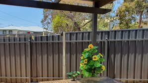 A wooden table with a potted plant and sunflowers in a covered outdoor area with a wooden fence in the background. - Rustic large 5 bedroom home in a inner city suburb (Enfield)