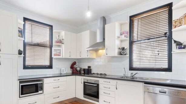 A modern kitchen with white cabinets, a wooden floor, a built-in oven, a microwave, and a dishwasher. - Rustic large 5 bedroom home in a inner city suburb (Enfield)