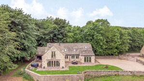 A stone house with a large patio, surrounded by dense trees. - Dog friendly holiday cottage in the Cotswolds with a hot tub - Owls Roost (Cold Aston, near Bourton-on-the-Water)